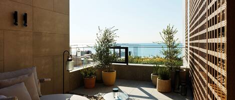 A modern balcony with a seating area, potted plants, and a view of the sea.