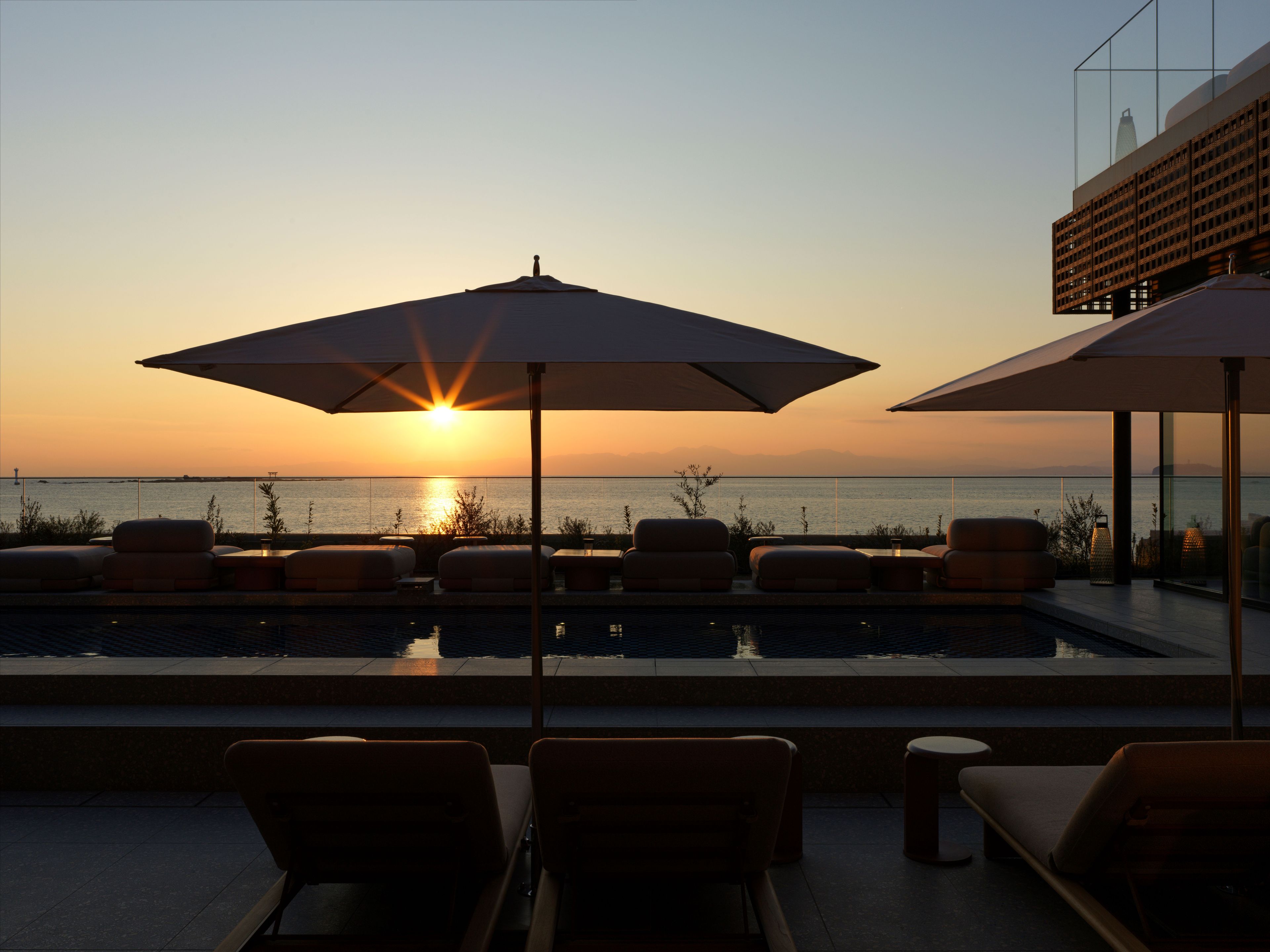 A poolside area with lounge chairs and umbrellas, overlooking a body of water during sunset.