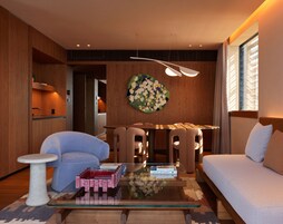 A modern living room with a sofa, armchairs, a coffee table, and a dining area with chairs.