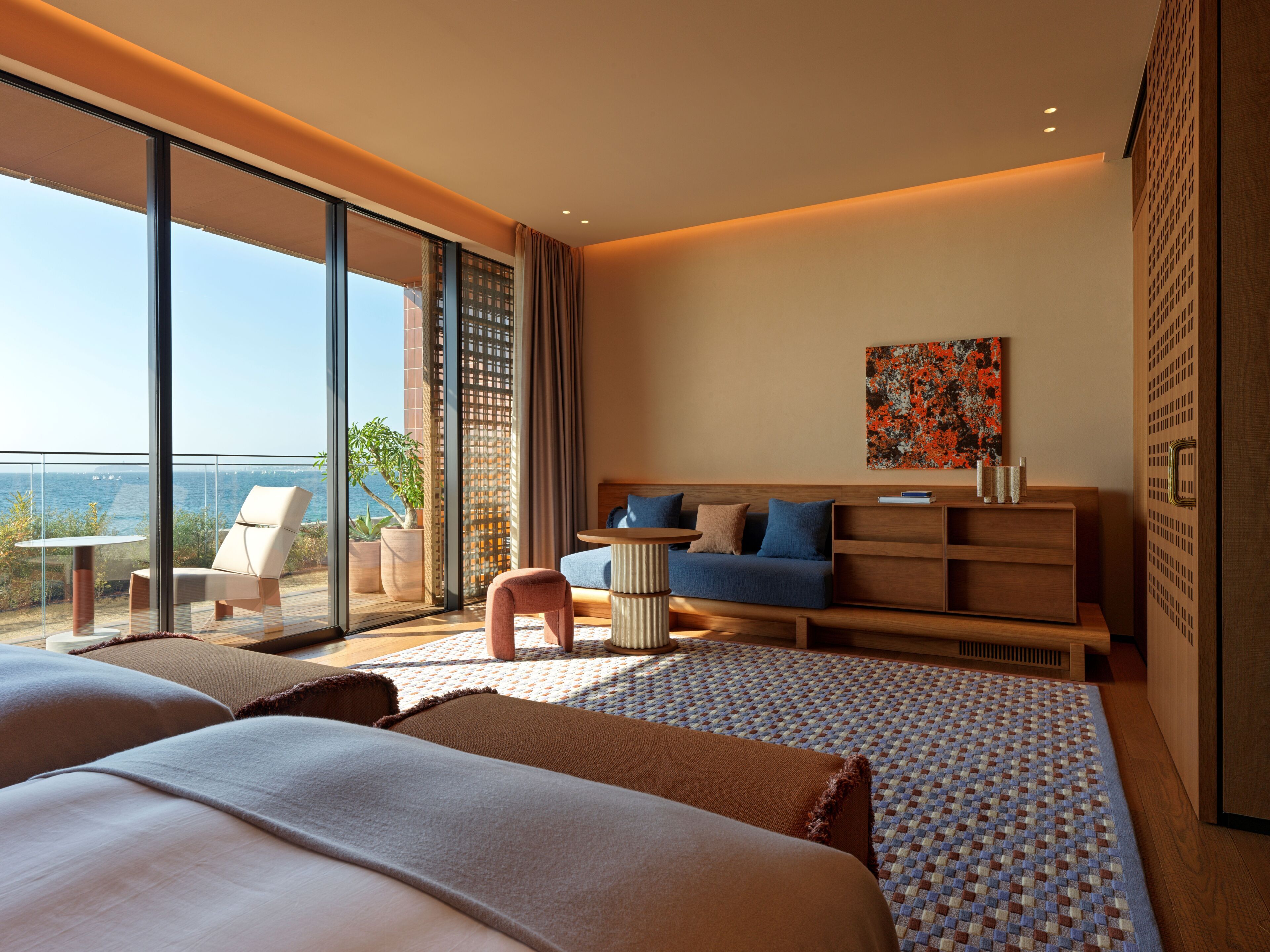 Habitación de hotel moderna con una cama grande, zona de estar con un sofá y sillones, una mesita y vistas al mar.