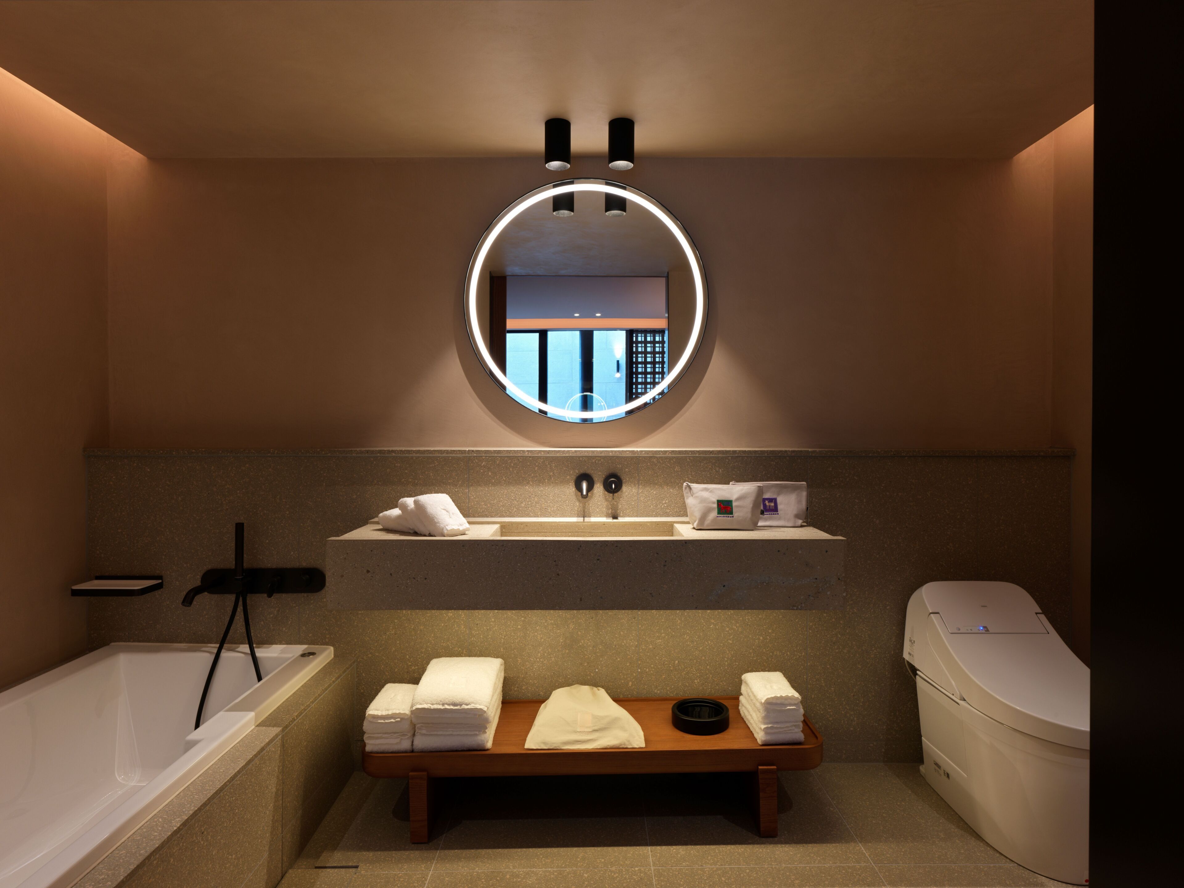 A modern bathroom with a bathtub, a round mirror, a sink, and a toilet.