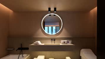 A modern bathroom with a bathtub, a round mirror, a sink, and a toilet.