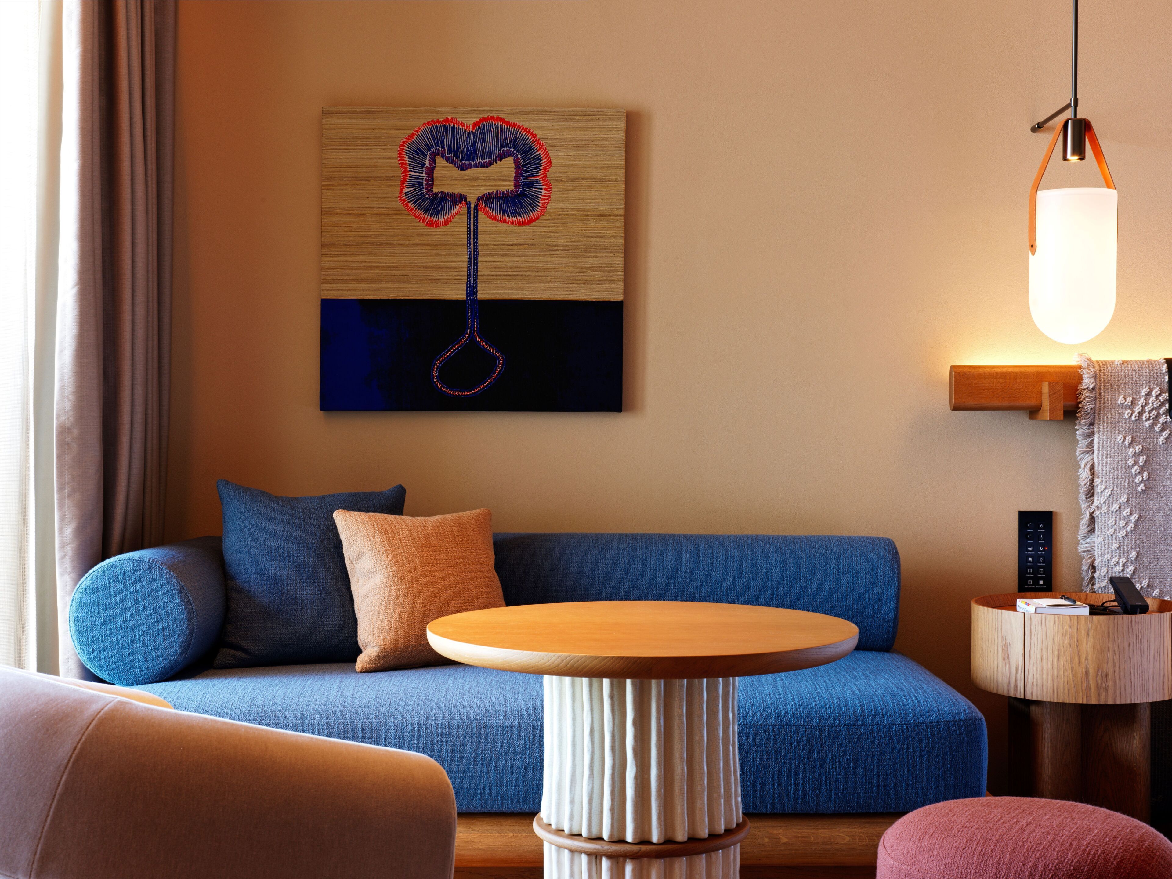 A modern living room with a blue sofa, a wooden coffee table, and a wall-mounted artwork.