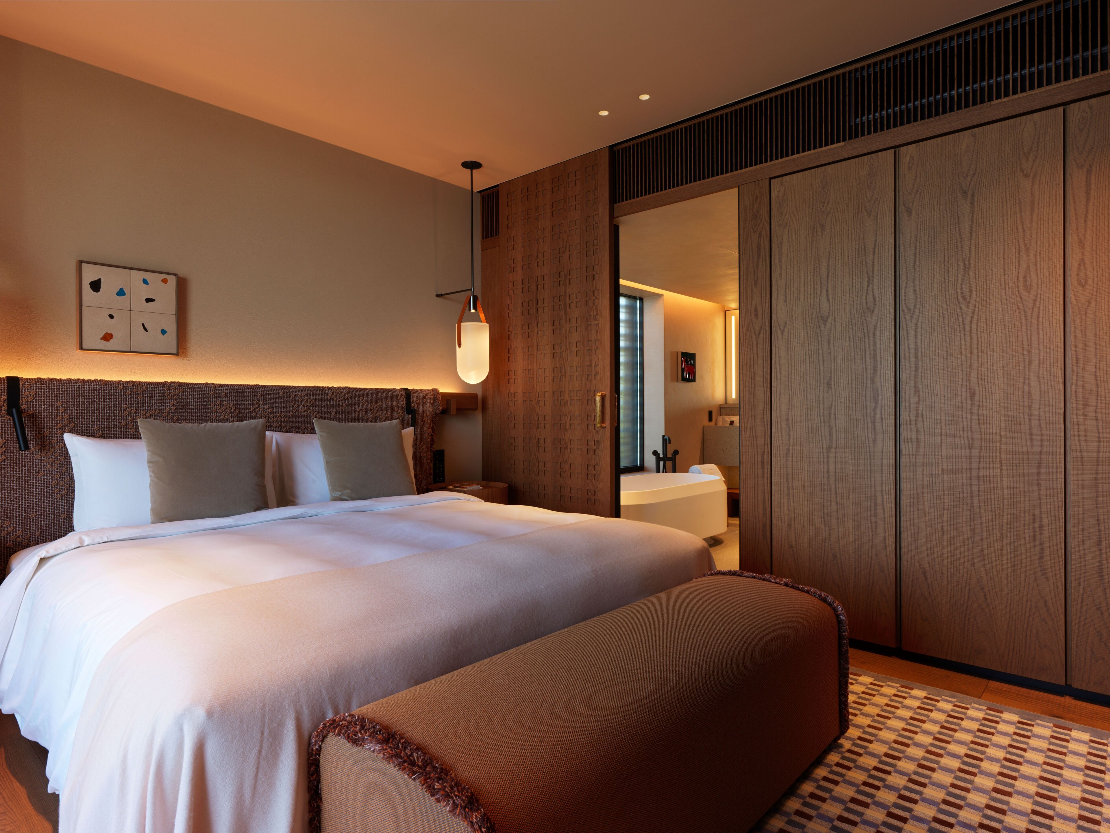 A hotel room with a large bed, a bedside table, a lamp, and a wardrobe.