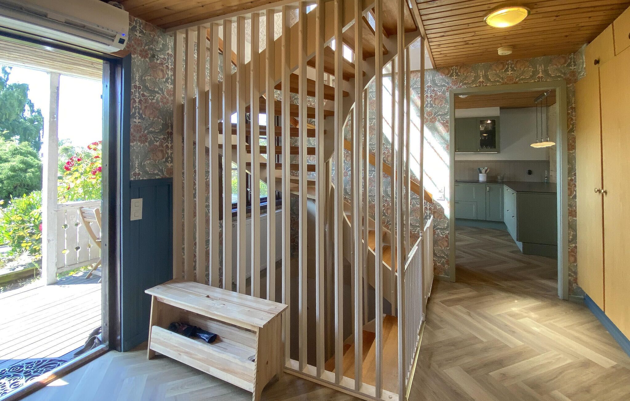 A room with a wooden floor, a built-in bench, a staircase, and a view of a garden.