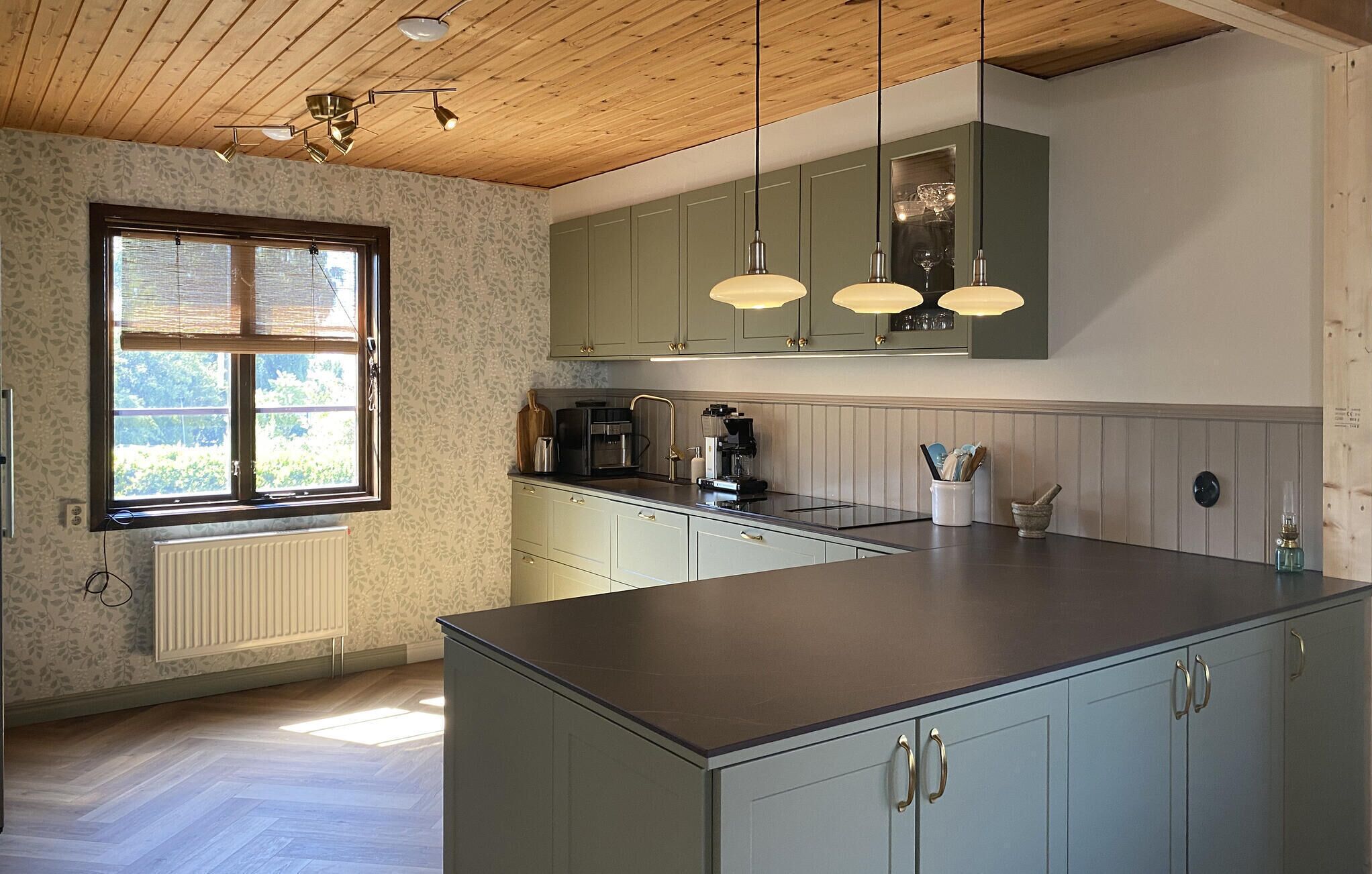 A modern kitchen with a central island, pendant lighting, and a window with blinds.