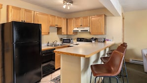 A kitchen with wooden cabinets, a black refrigerator, a microwave, a stove, and a bar area with chairs. - Ski In/Out|Hot Tub|Great Views|Walk to Base Area (Steamboat Springs)