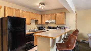 A kitchen with wooden cabinets, a black refrigerator, a microwave, a stove, and a bar area with chairs.
