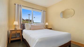 Un dormitorio con una cama grande, dos mesitas de noche con lámparas, una ventana con cortinas y un espejo montado en la pared.