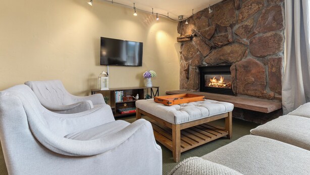 A living room with a stone fireplace, a flat-screen TV mounted on the wall, and a comfortable seating area with modern sofas. - Ski In/Out|Hot Tub|Great Views|Walk to Base Area (Steamboat Springs)