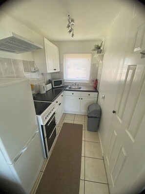 A compact kitchen with white cabinets, a stove, a microwave, and a sink. - Comfortable & homely 2-bed Chalet with FREE passes to swimming pool, gym & club (GREAT YARMOUTH)