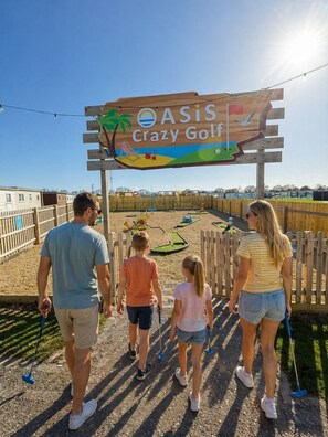 A family walking towards a golf course sign with a tropical theme. - Comfortable & homely 2-bed Chalet with FREE passes to swimming pool, gym & club (GREAT YARMOUTH)