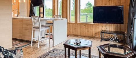 En inredning med träpanel, bestående av ett kök, en matplats och ett vardagsrum, med en TV, glasbord och en soffa.
