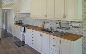 Una cocina con armarios blancos, encimera de madera, pileta y salpicadero.