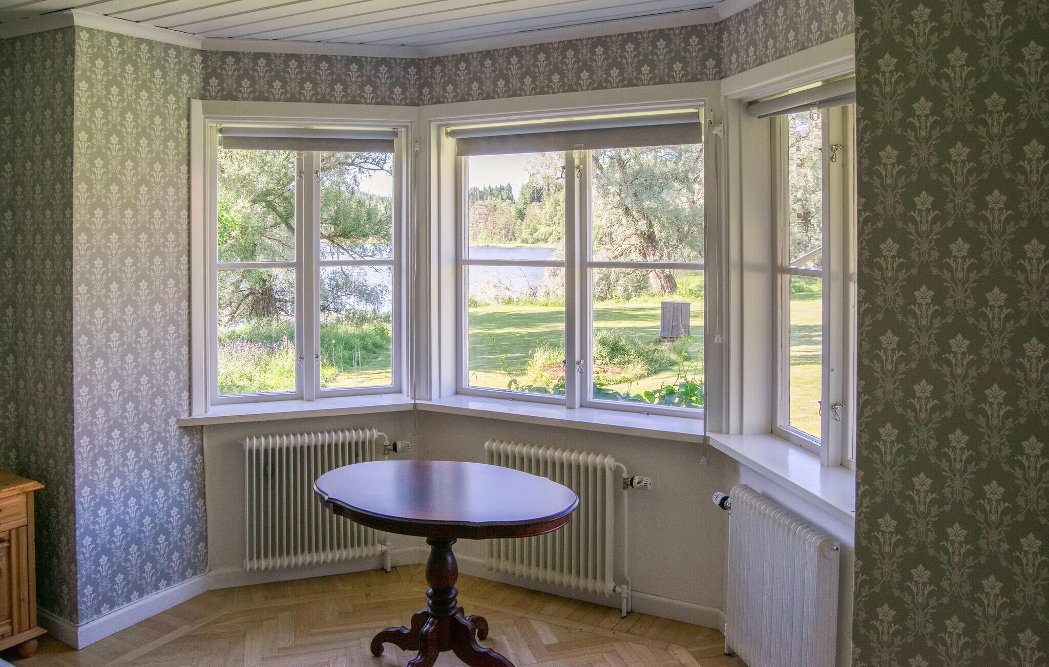 Quarto com janela panorâmica, radiador e uma mesa.