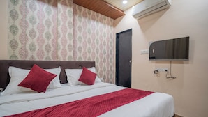 A hotel room with a bed, a television mounted on the wall, and a patterned wallpaper. - Hotel Misty Prime (Indore)