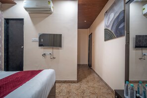 A hotel room with a bed, a mirror, an air conditioner, a door, and a hallway leading to another room. - Hotel Misty Prime (Indore)