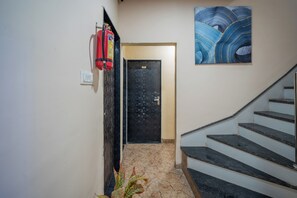 A staircase with a handrail, a fire extinguisher mounted on the wall, and a door with a number plate. - Hotel Misty Prime (Indore)