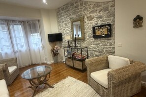 A living room with wicker furniture, a glass coffee table, a stone wall, a flat-screen TV, and a mirror. - 1A172 Quiet Apartment in Gijón (Gijón)