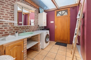 A compact bathroom with a sink, mirror, washing machine, and a wooden door. - Maison de vacances à Saint-Valéry-sur-Somme (Saint-Valery-sur-Somme)