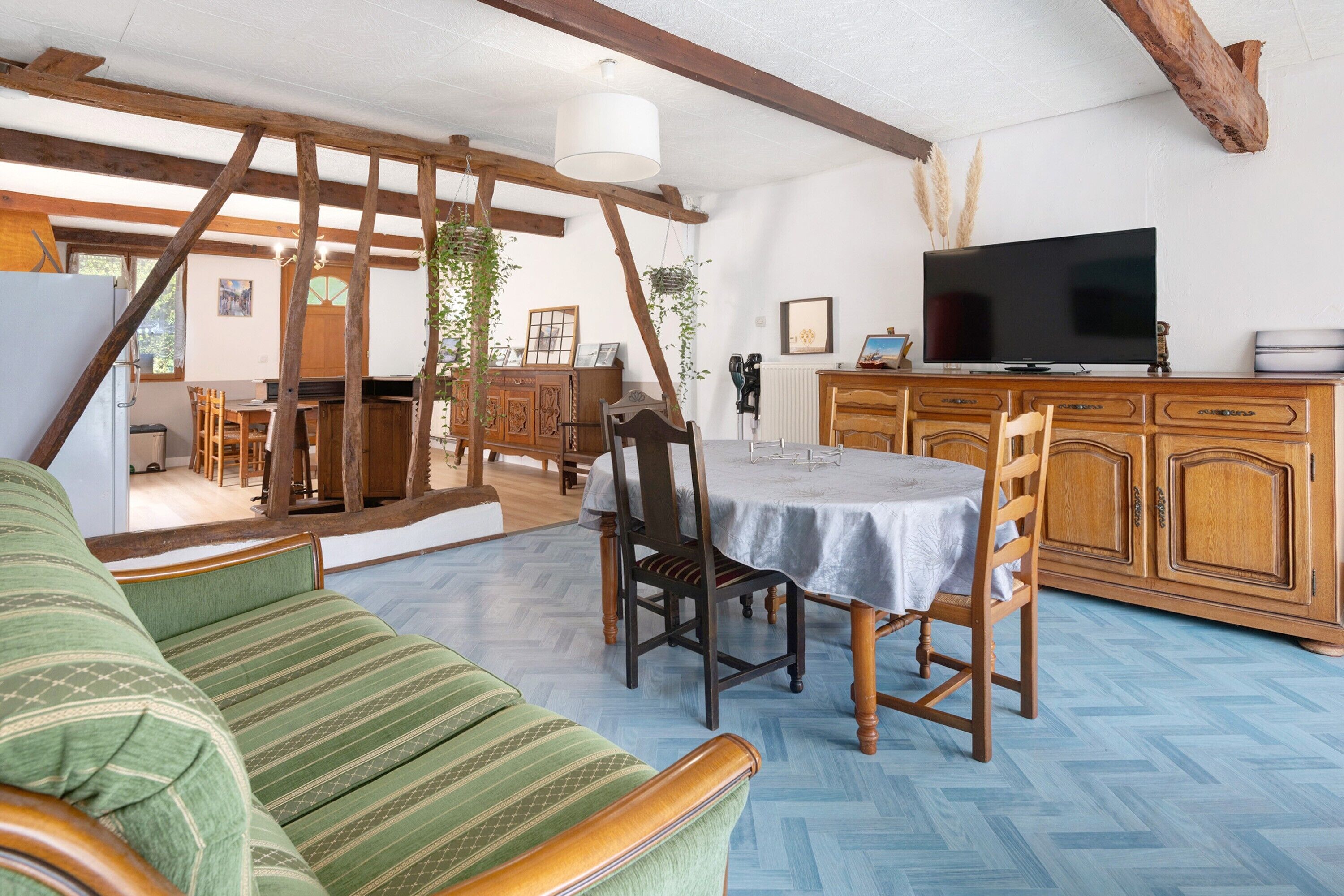 A cozy living room with a sofa, a dining table with chairs, a television, and wooden cabinets.