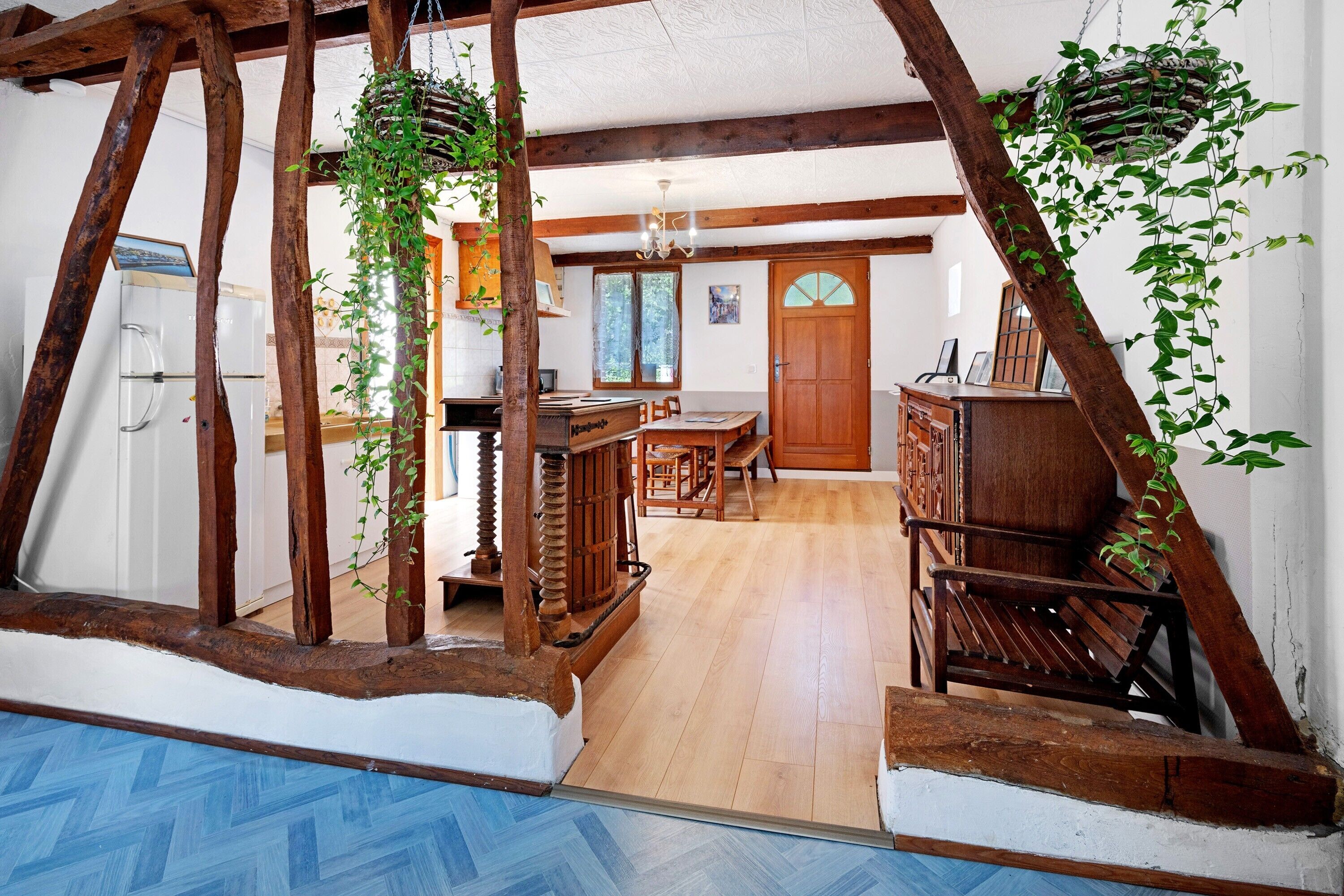 Un intérieur rustique avec des poutres apparentes, une table en bois entourée de chaises et des plantes suspendues.