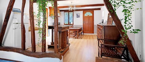 A rustic interior with exposed wooden beams, a wooden table with chairs, and hanging plants.