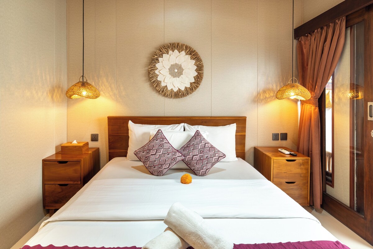 A neatly made bed with two pillows, a bedside table with a remote control, and a wall-mounted decorative piece.