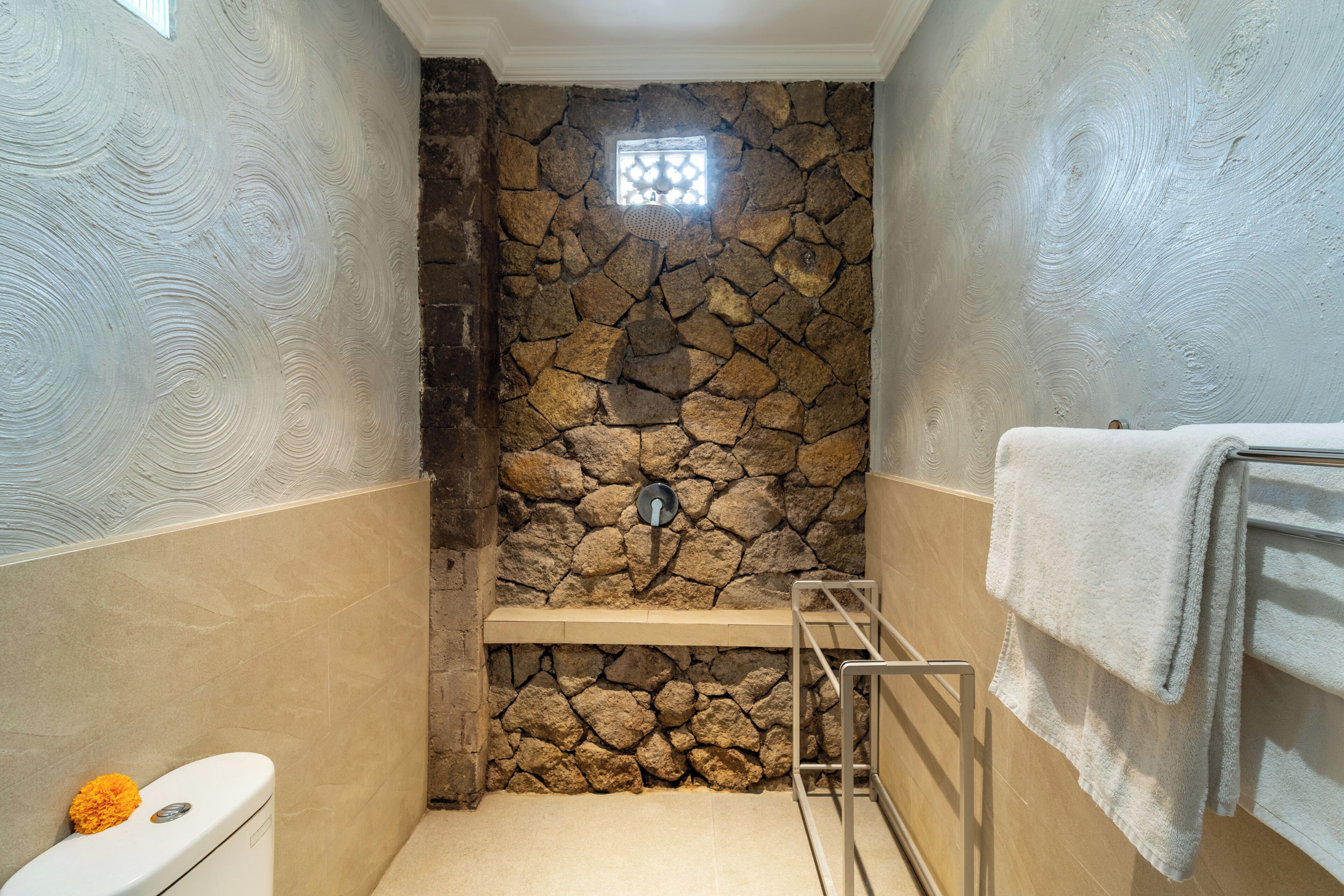 Une salle de bain avec un mur en pierre, des toilettes, un porte-serviettes et une fenêtre.