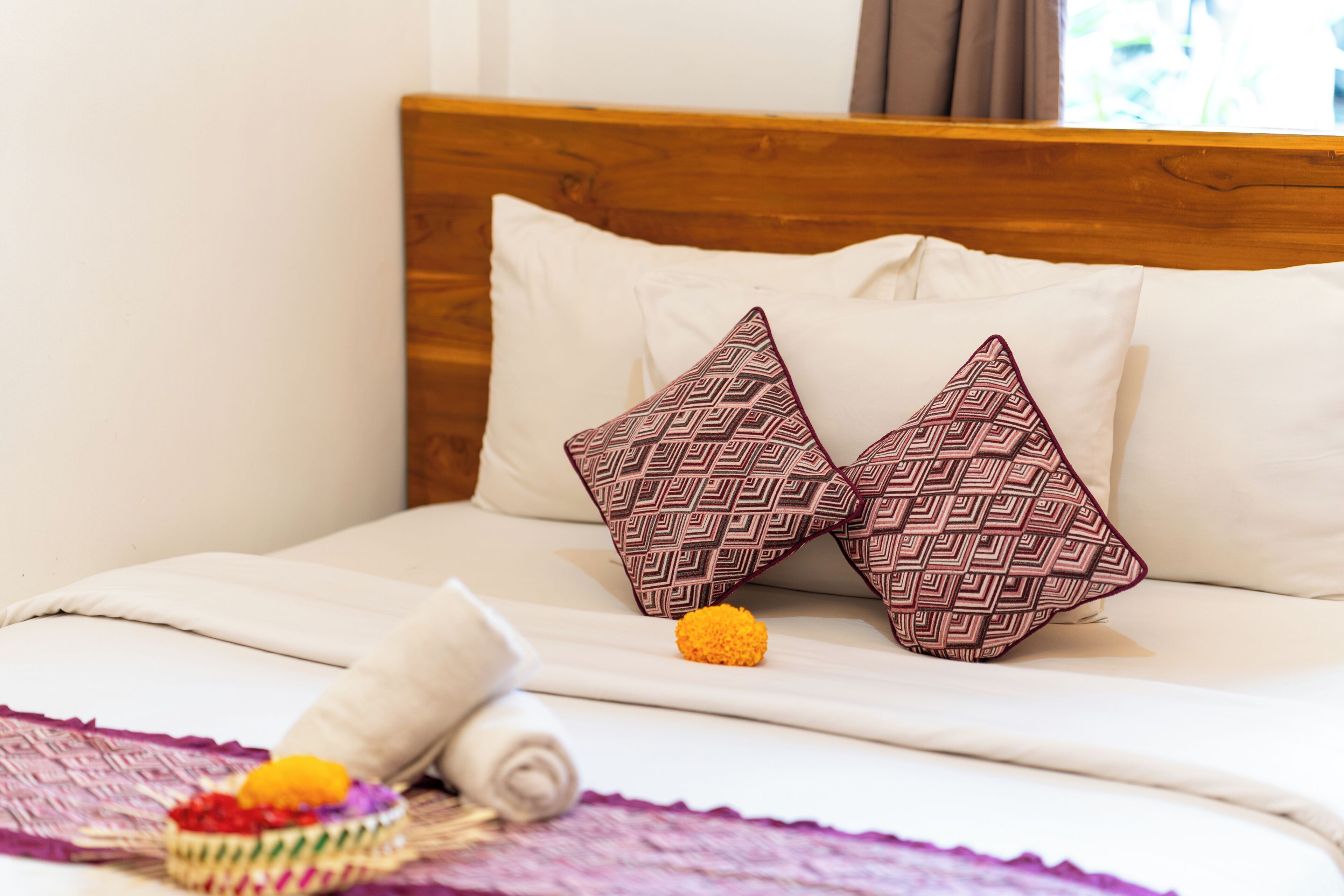 Un lit avec deux oreillers à motifs, une serviette enroulée et un petit panier rempli de fruits.