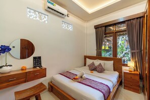 A hotel room with a bed, bedside table, a mirror, a dresser, and a window with curtains. - Ubud Heritage Stay (Gianyar)