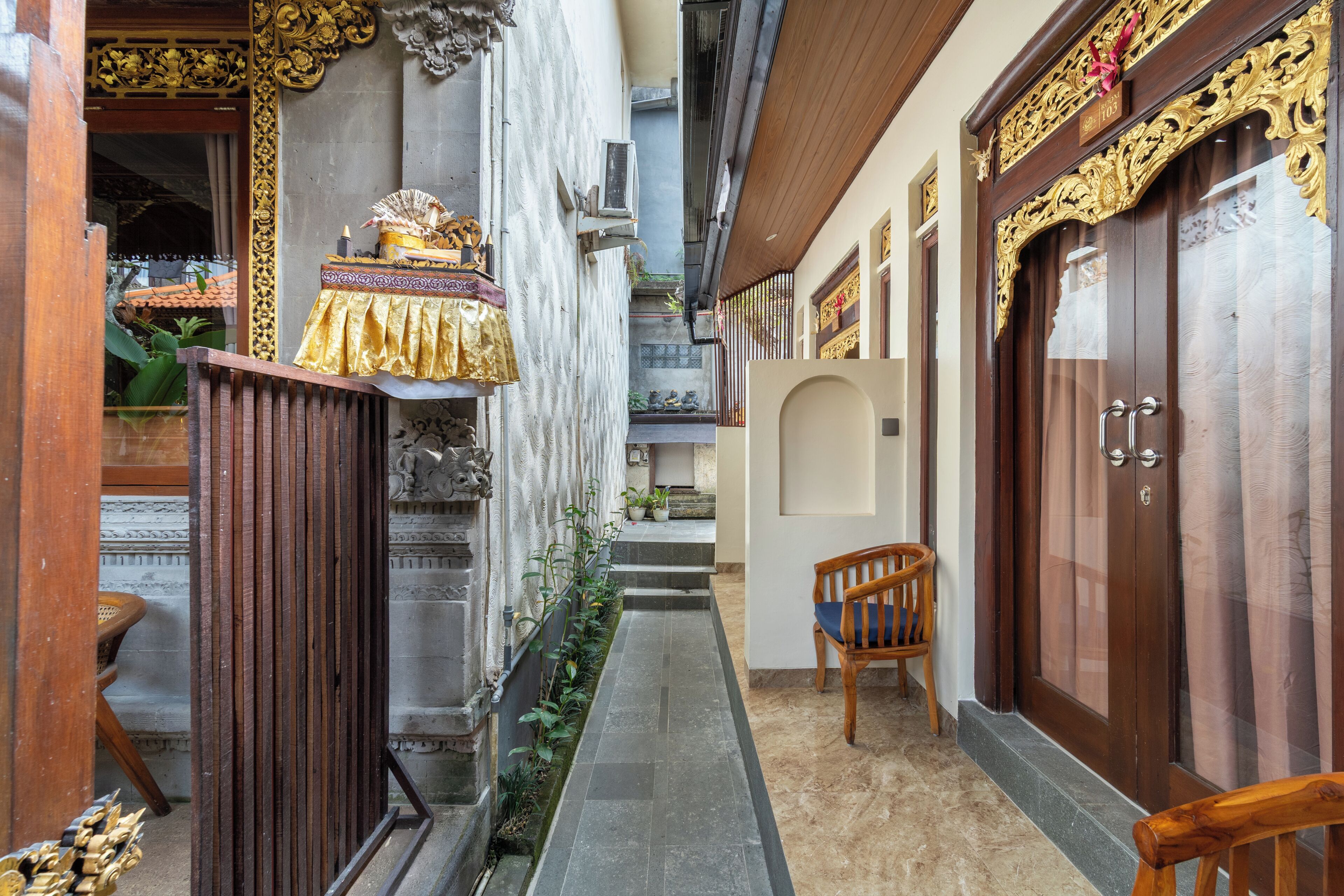 A narrow alleyway with a wooden bench, a door with ornate carvings, and a small staircase leading to a higher level.
