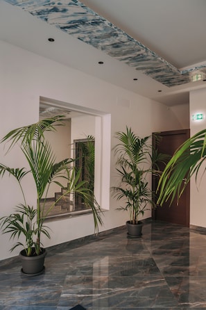 A hallway with marble flooring, potted plants, and a ceiling with a blue abstract design.