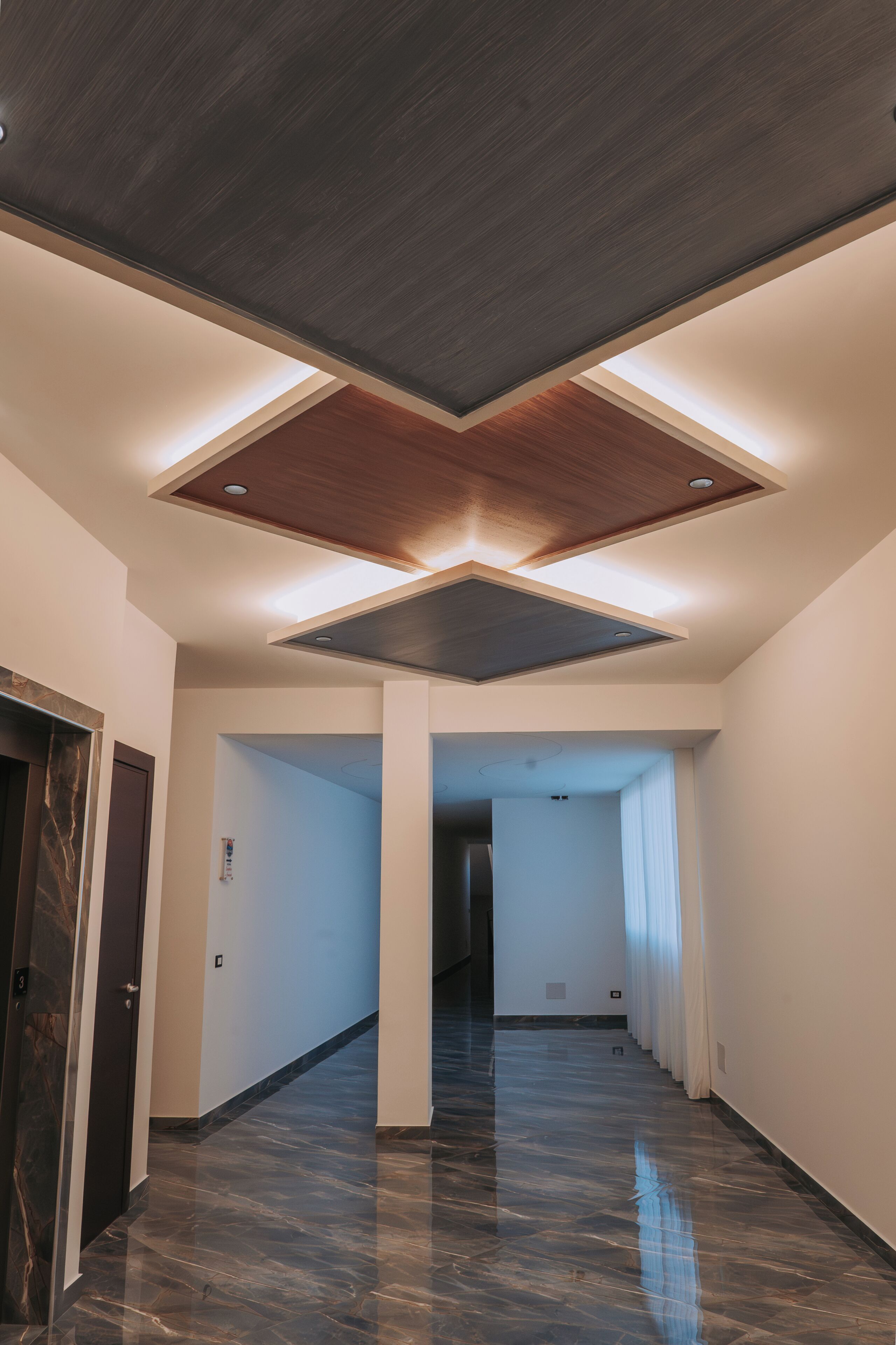 Un corridoio con pavimento in marmo lucido, soffitto in legno con decorazioni e una porta a sinistra.