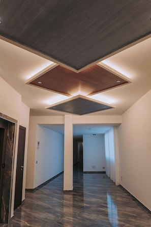 A corridor with a polished marble floor, a wooden ceiling design, and a door on the left.