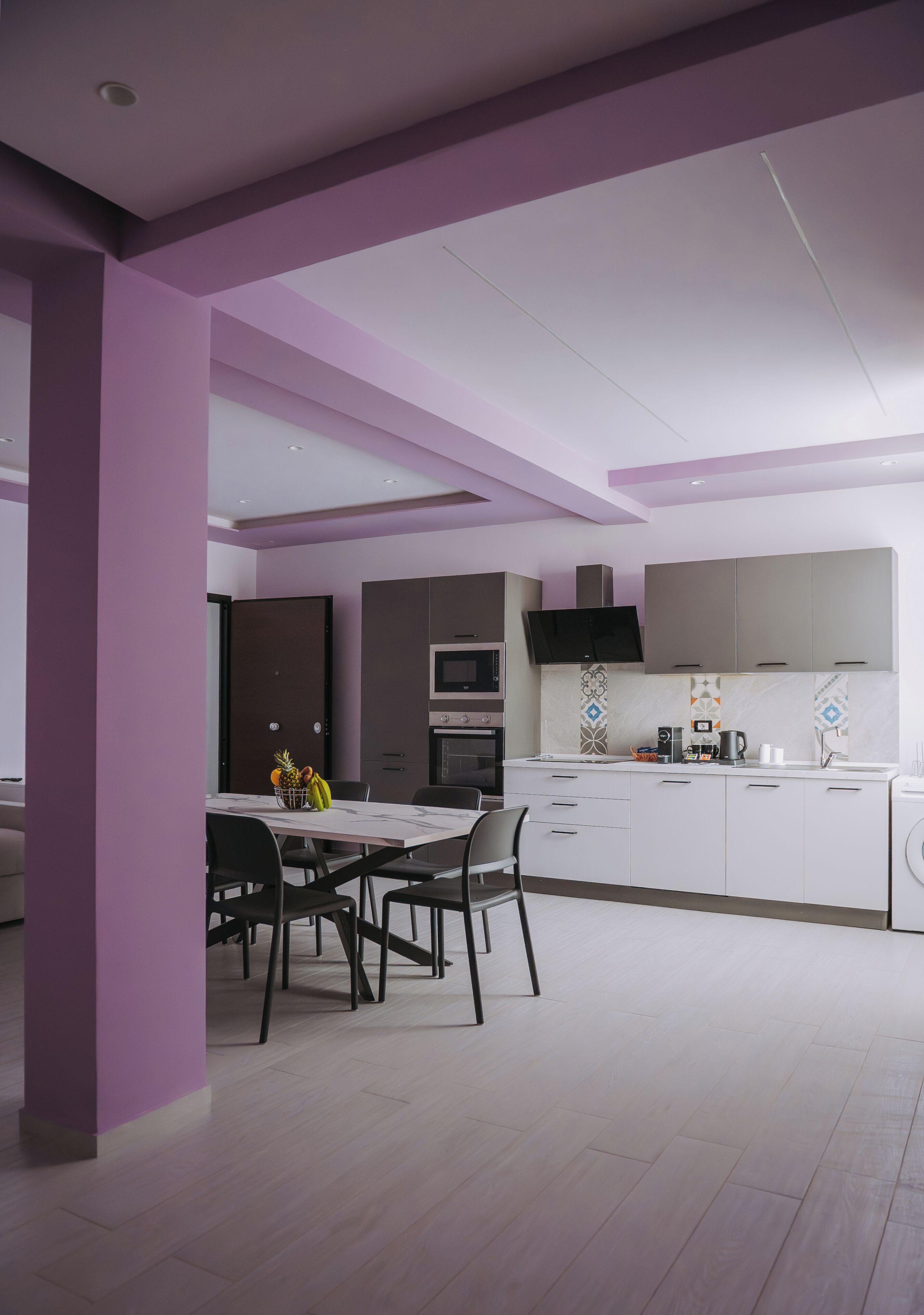A modern kitchen with white cabinets, a dining area with a table and chairs, and a large window.