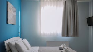 A modern bedroom with a bed, bedside table, and a TV on the wall.