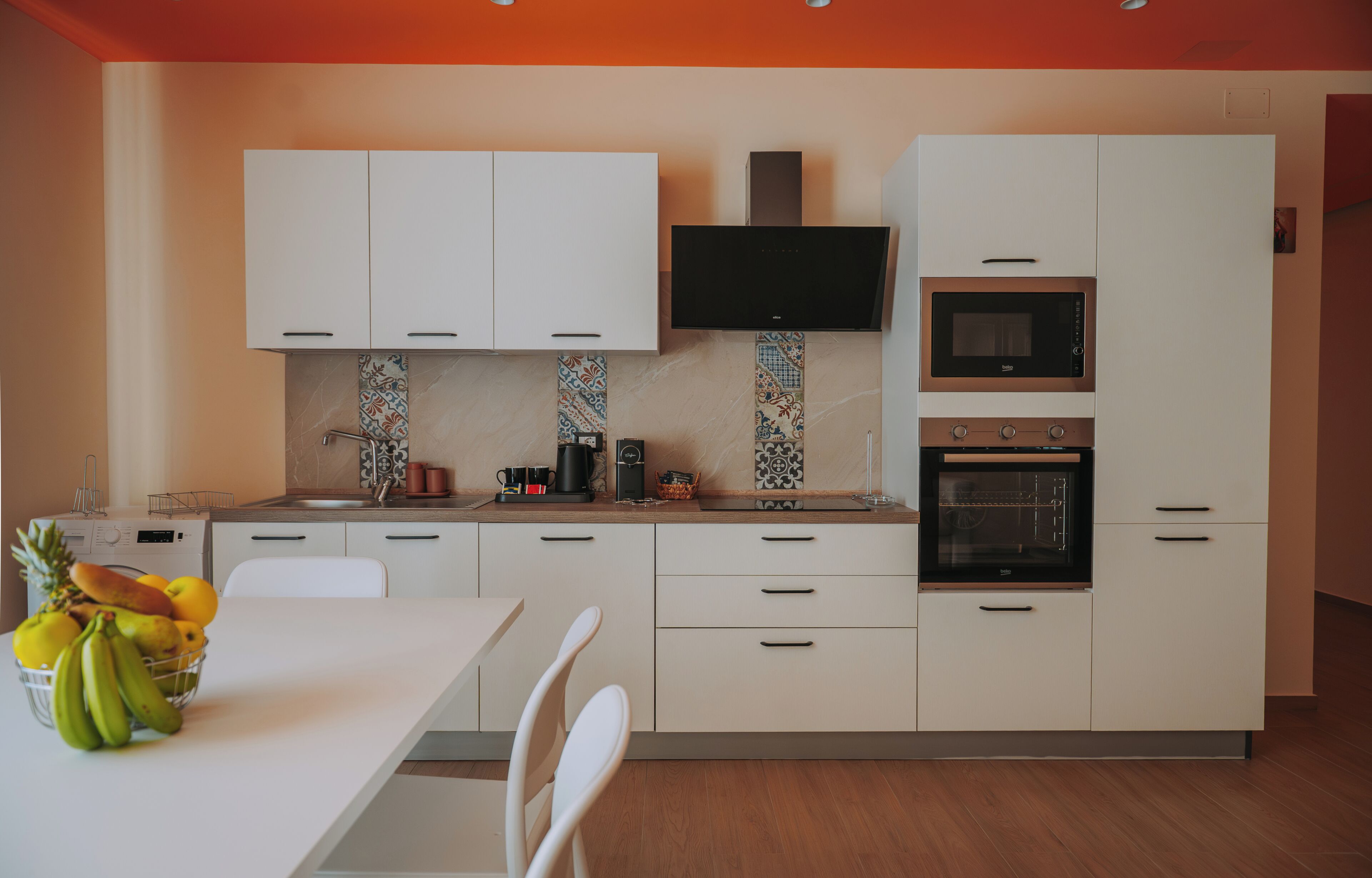 Een kleine keuken met witte kastjes, een flatscreen televisie, een magnetron en een oven.