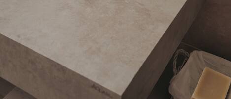 Un baño con un lavamanos grande blanco, un dispensador de jabón y un pequeño jabonero rectangular sobre una encimera color beige.