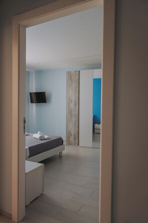 A modern bedroom with a bed, a flat-screen TV mounted on the wall, and a wooden wardrobe.