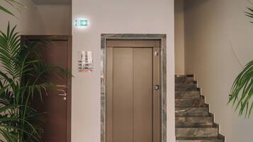 Una hall con pavimento in marmo, una porta in legno, una scalinata e un soffitto decorato con un motivo blu e bianco.