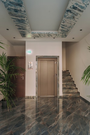 A lobby with a marble floor, a wooden door, a staircase, and a ceiling with a blue and white pattern.