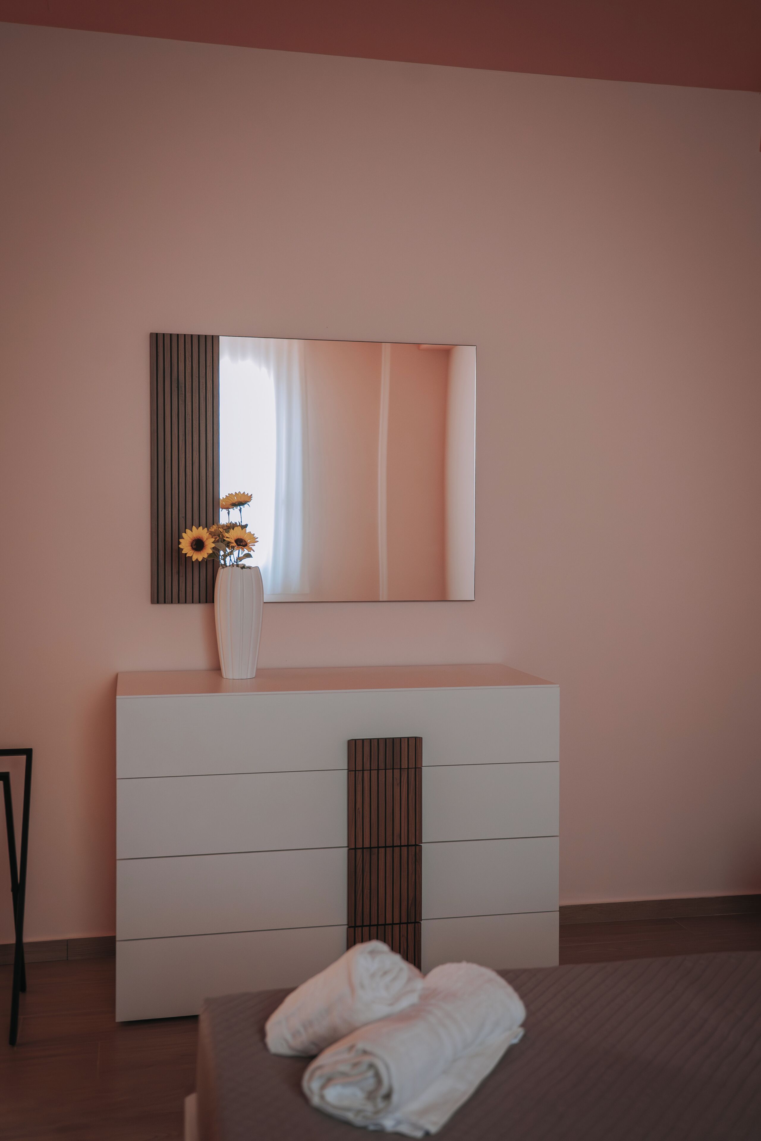Een moderne slaapkamer met een grote spiegel, een witte dressoir en een bed met opgerolde handdoeken.