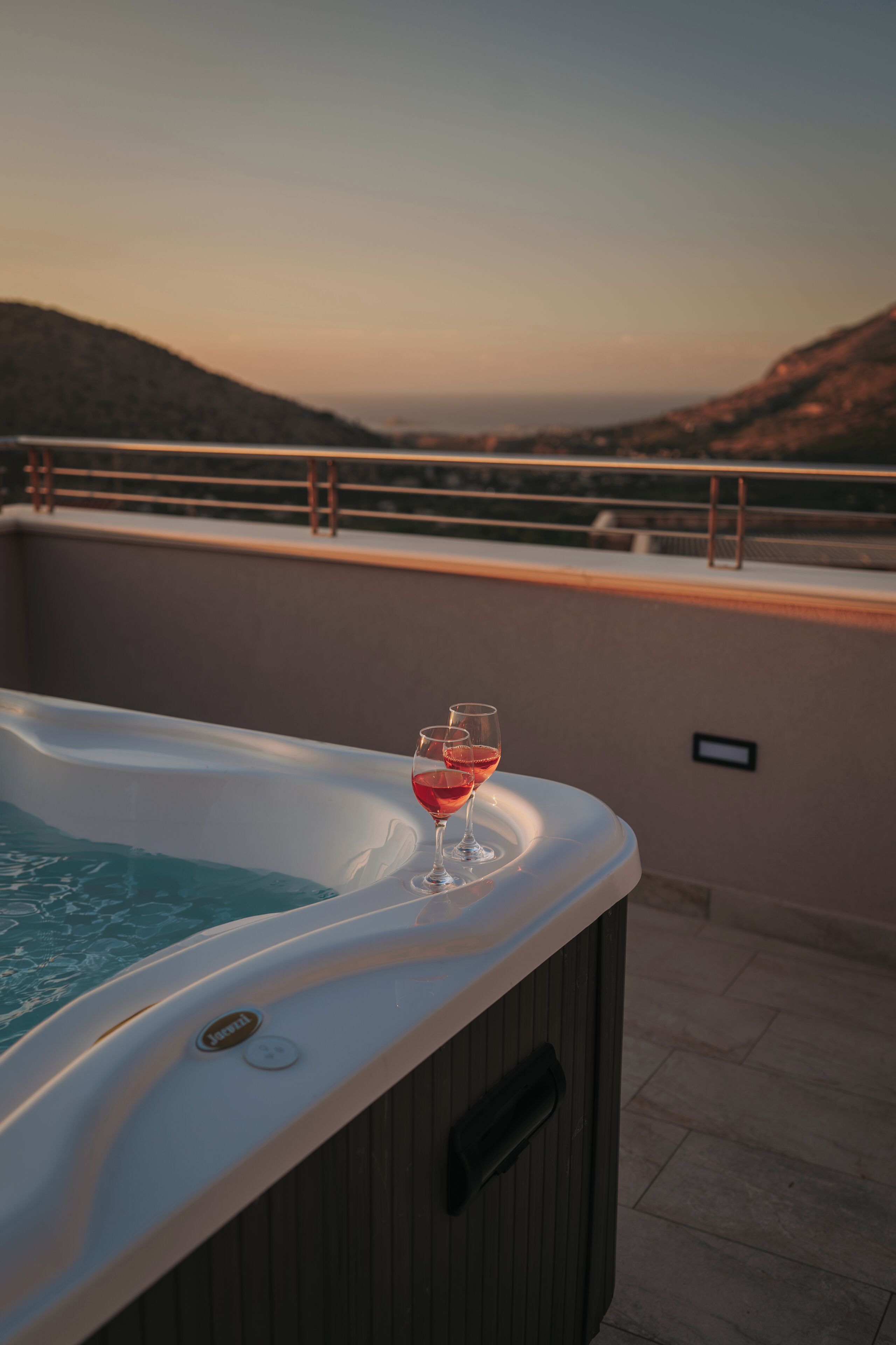 Ein Whirlpool mit einem Glas Rotwein auf einem Balkon mit Blick auf eine gebirgige Landschaft.