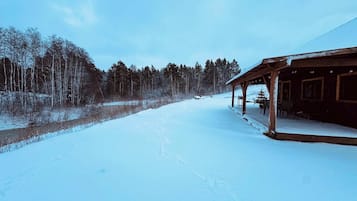A snow-covered landscape with a wooden cabin featuring a porch and a small Christmas tree.