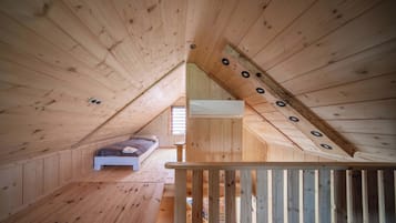 A wooden attic bedroom with a sloped ceiling, a single bed, and a window.