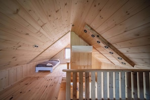 A wooden attic bedroom with a sloped ceiling, a single bed, and a window.