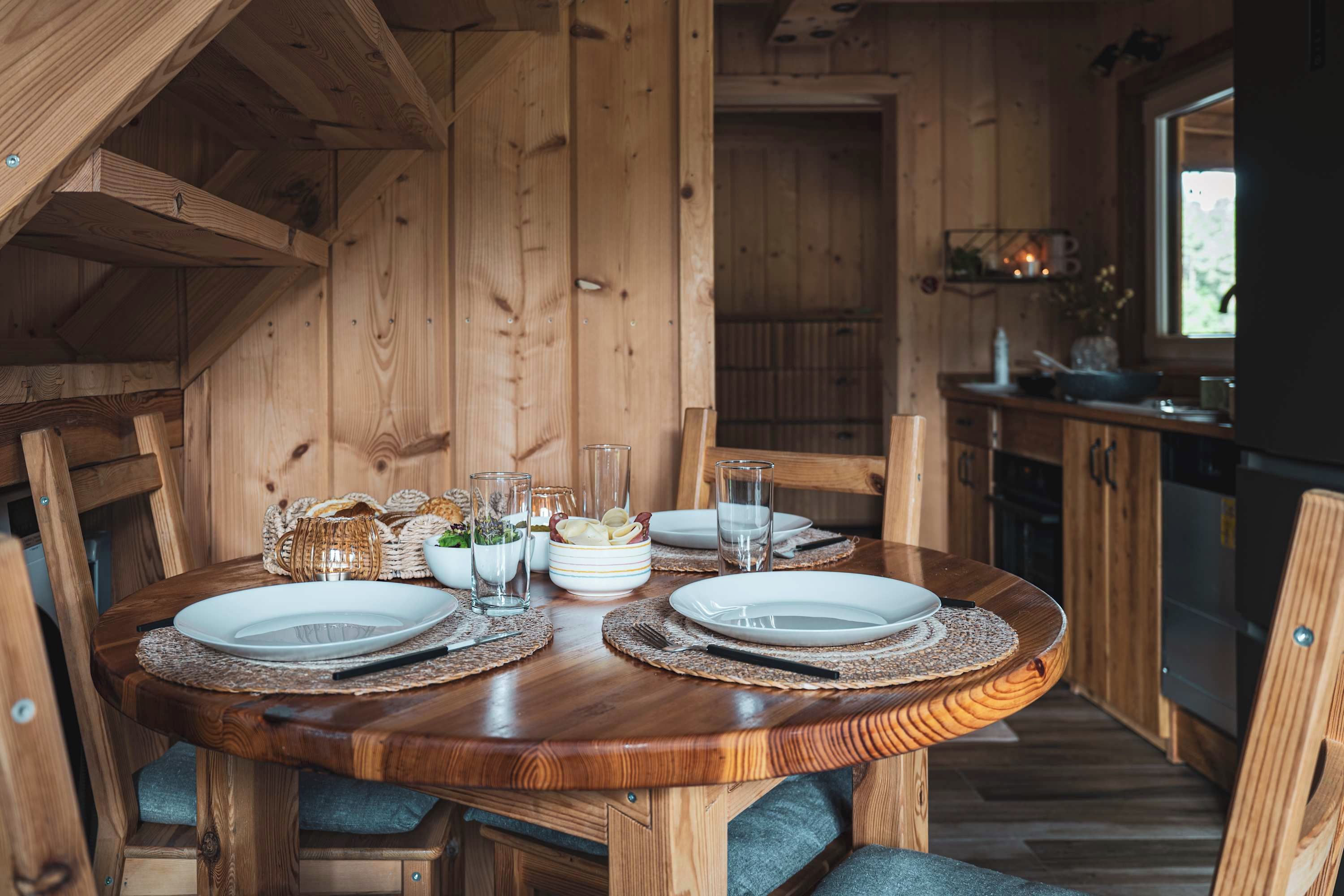 A wooden dining table set with plates, glasses, and a woven placemat.