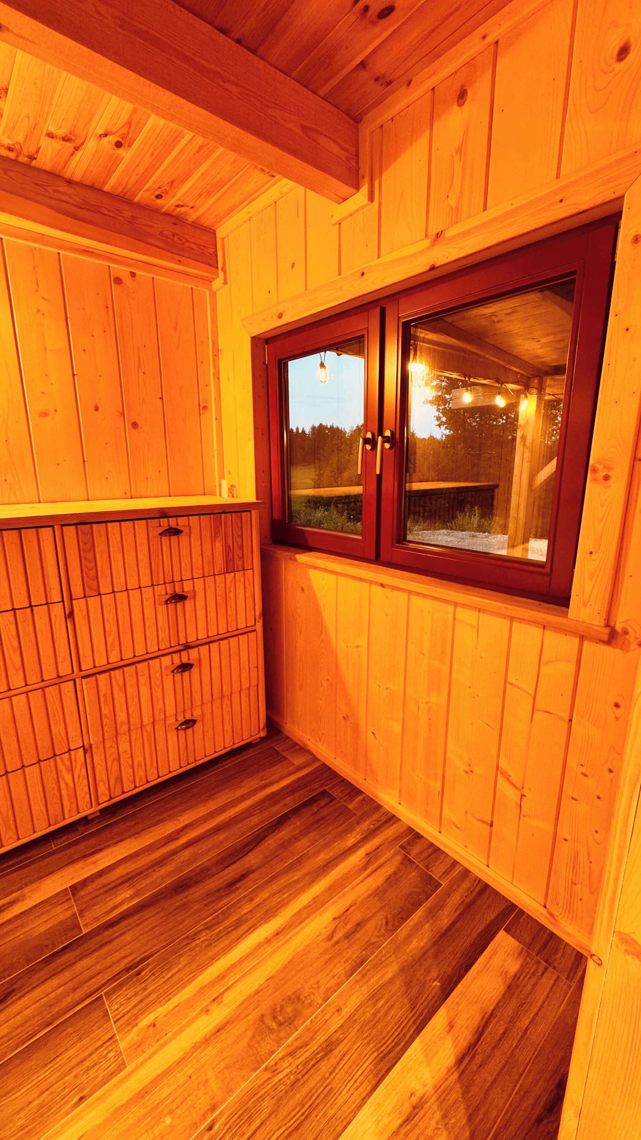A room with wooden walls, a window with a view of the outdoors, and a wooden cabinet.