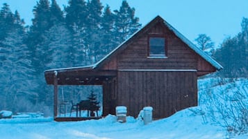 A wooden cabin with a covered porch, surrounded by snow and trees.